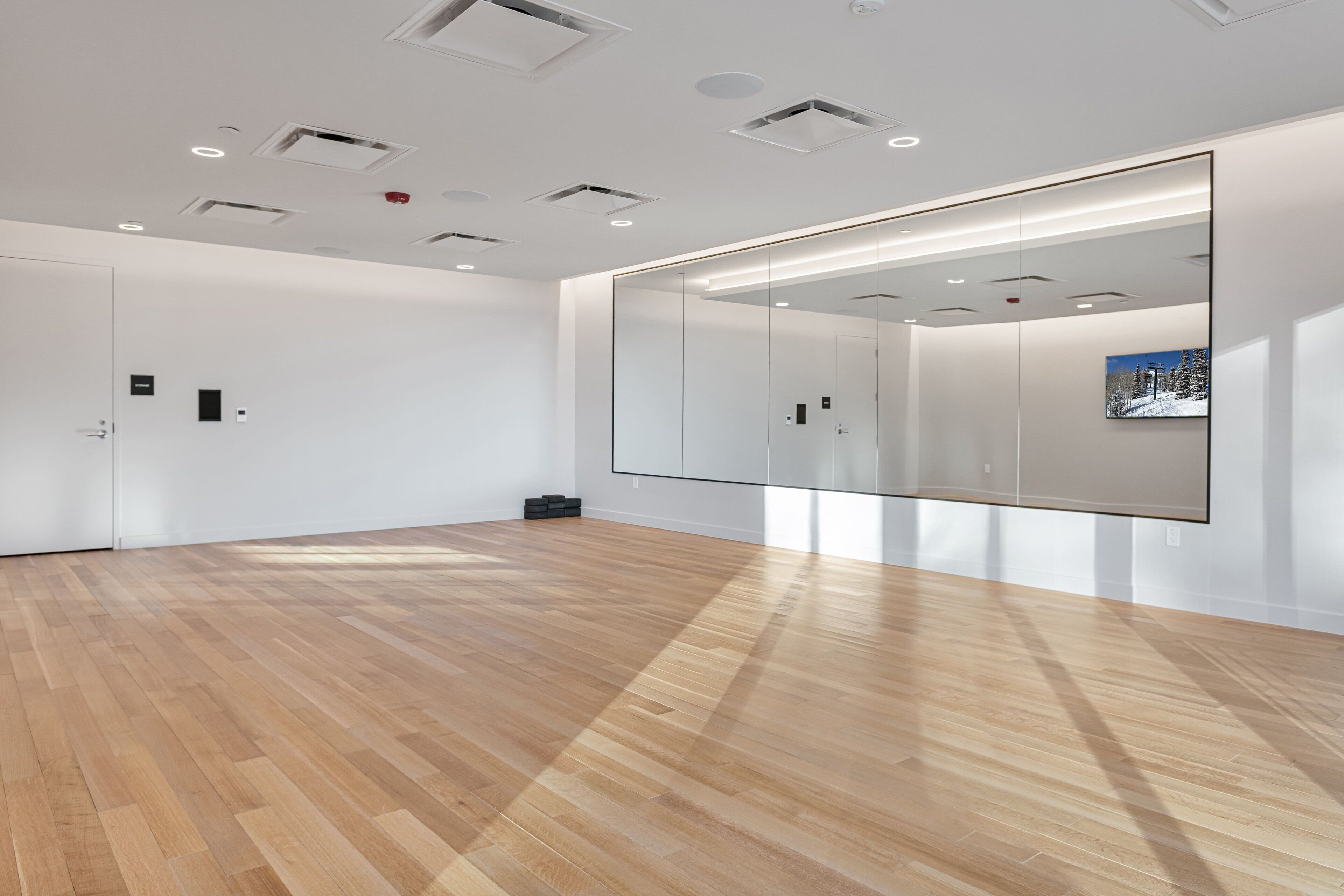 Una habitación amplia con un espejo grande, suelo de madera y luces empotradas en el techo.