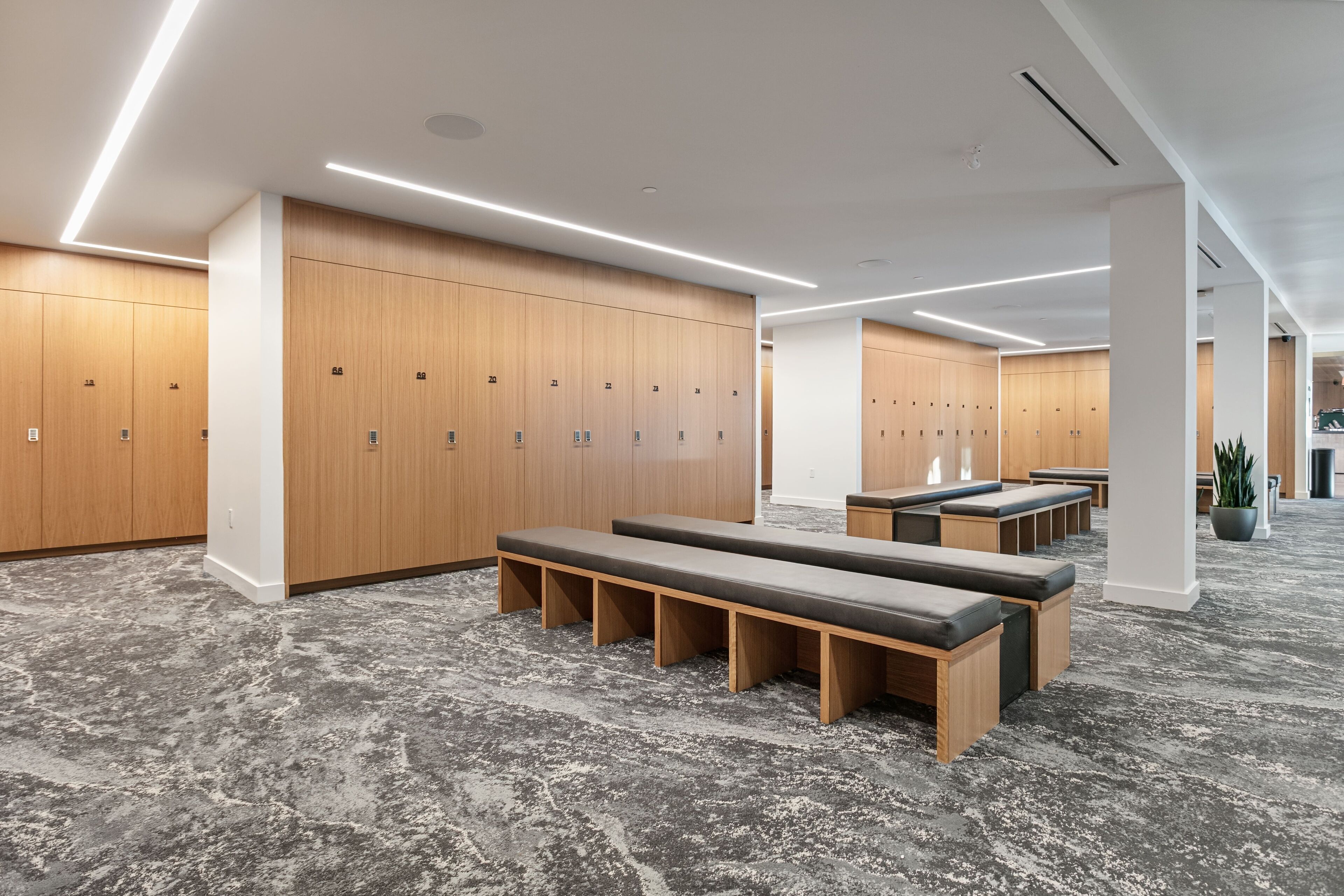 A modern locker room with wooden lockers, benches, and a grey textured floor.