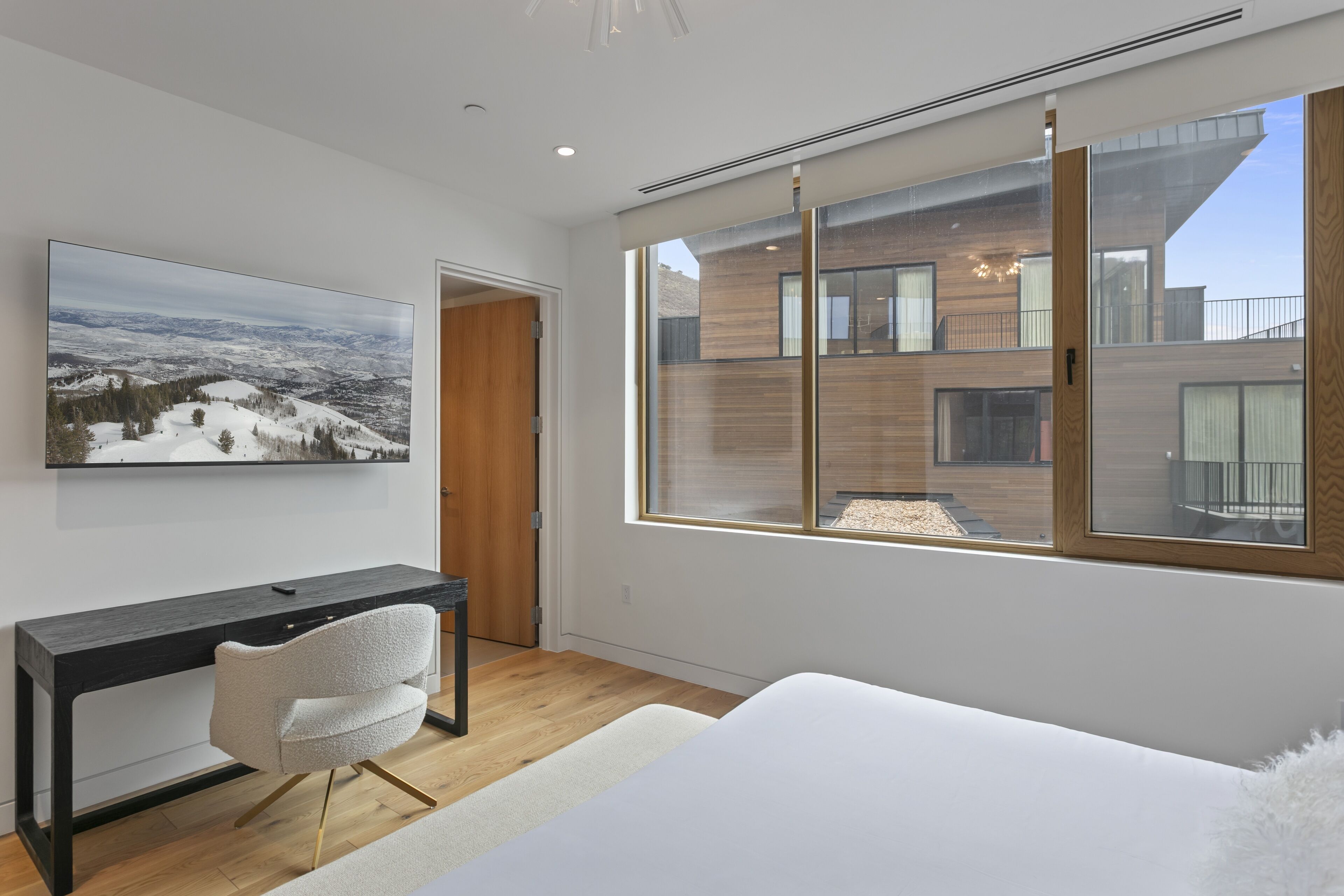 Ein modernes Schlafzimmer mit einem großen Bett, einem Schreibtisch und einem großen Fenster mit Blick auf ein modernes Gebäude.