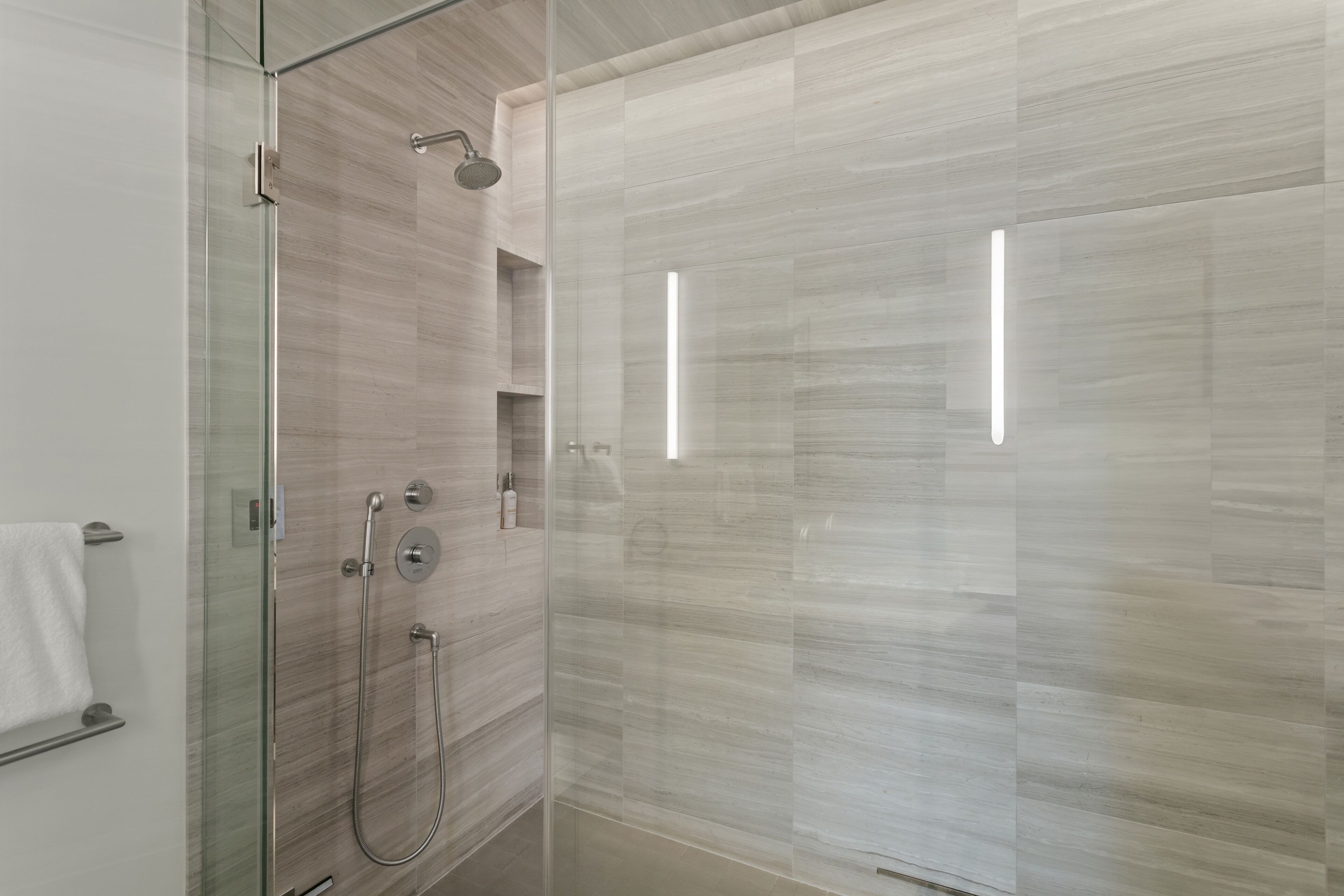 A modern bathroom with a glass-enclosed shower, a towel rack, and a built-in shelf.