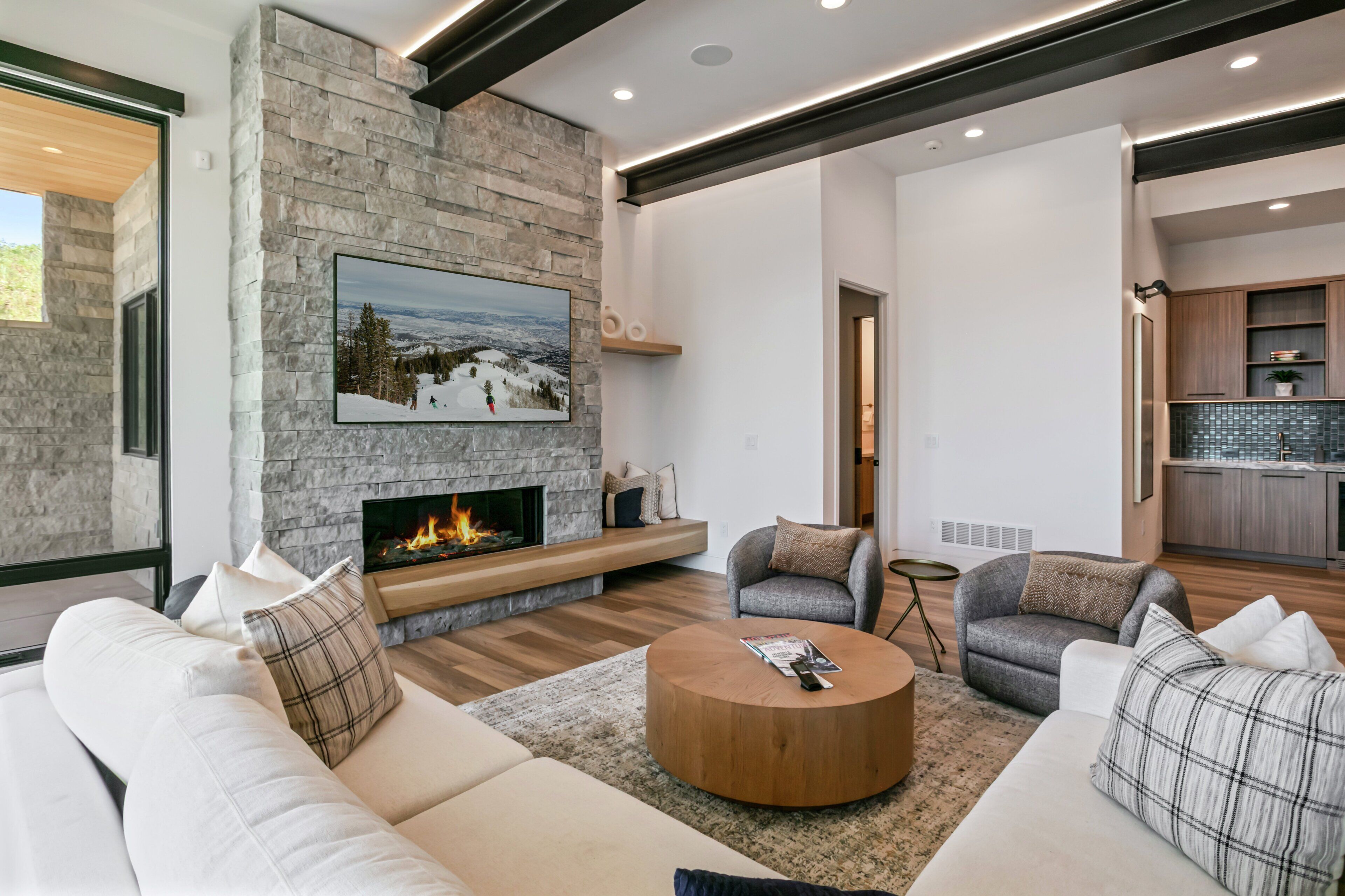 A modern living room with a stone fireplace, a large flat-screen TV, and a cozy seating area.