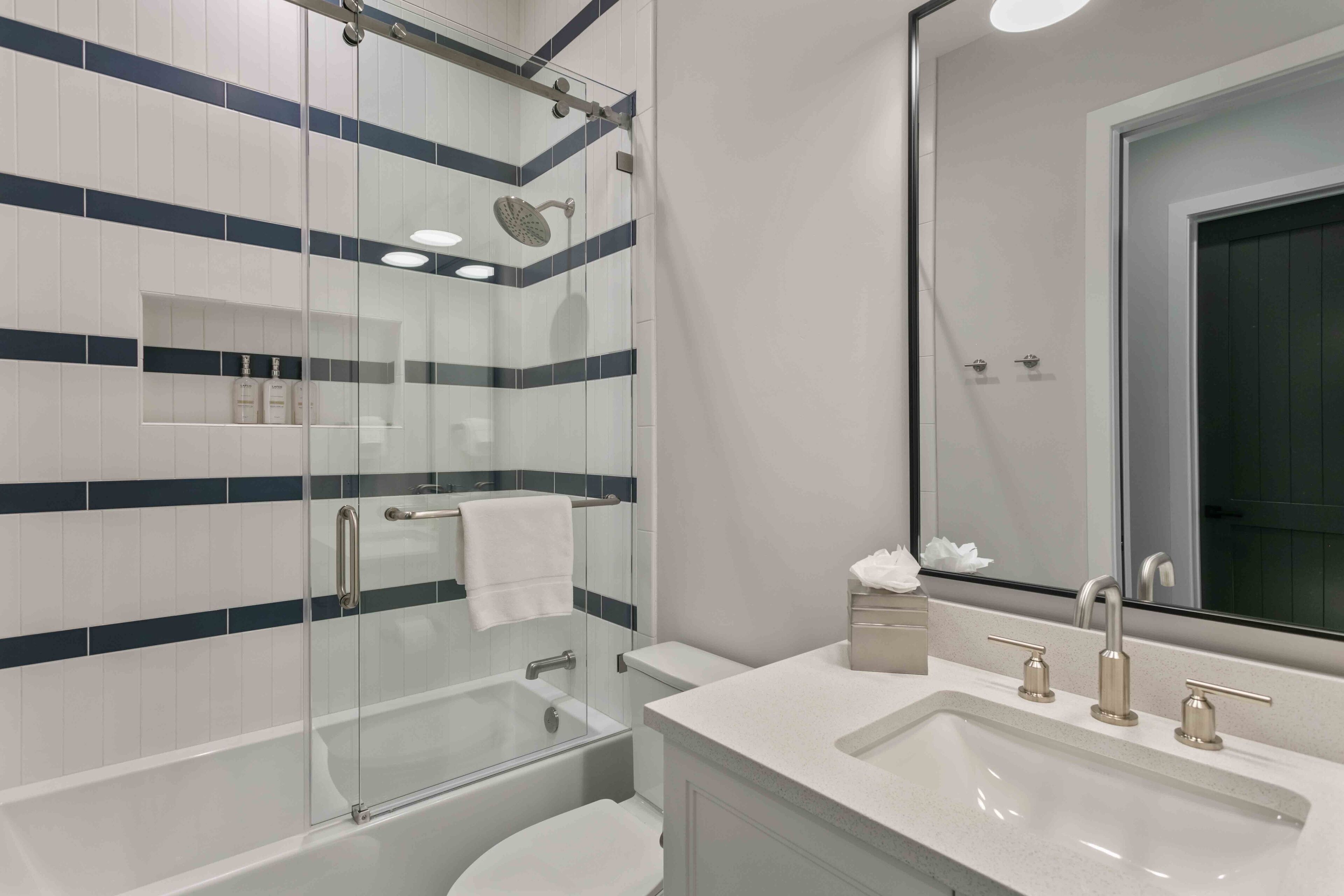 Un baño moderno con cabina de ducha de vidrio, un lavamanos blanco con doble grifo y un espejo grande.