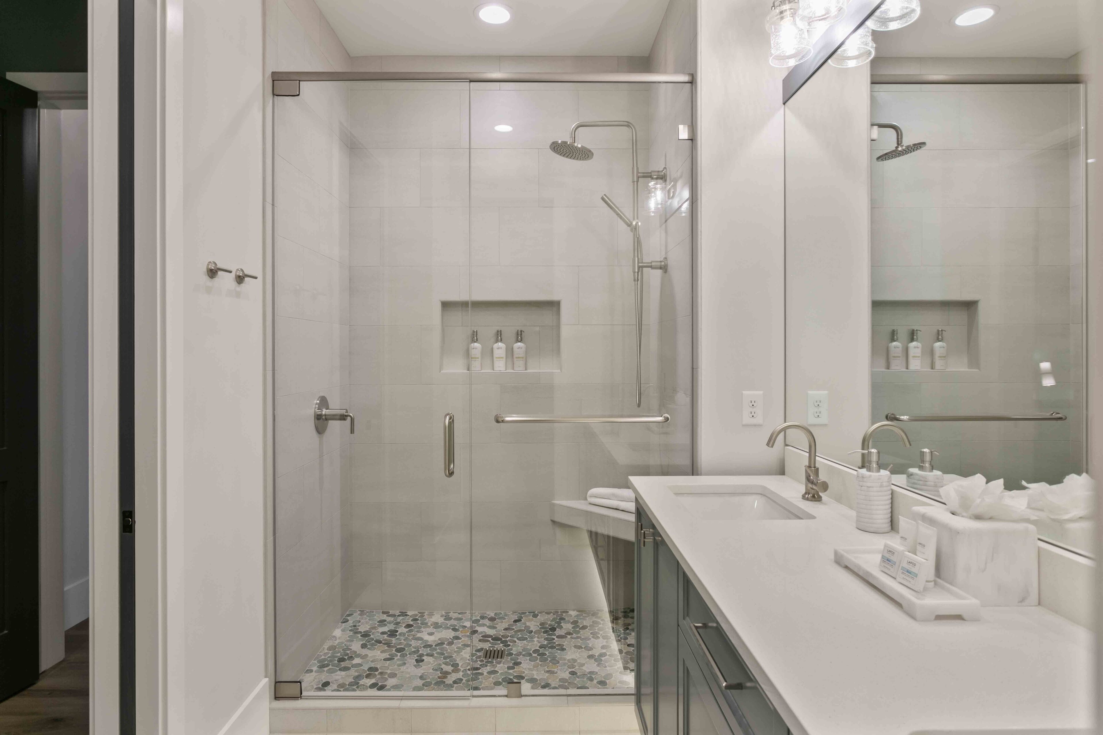 A modern bathroom with a glass-enclosed shower, a vanity with a sink, and a mirror.