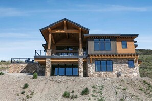 A modern two-story house with a stone facade, large windows, and a prominent wooden balcony. - 11981 N Gemini Way Skyridge 5 Bedroom Home With Hot Tub by Deer Valley Resort (Heber City)