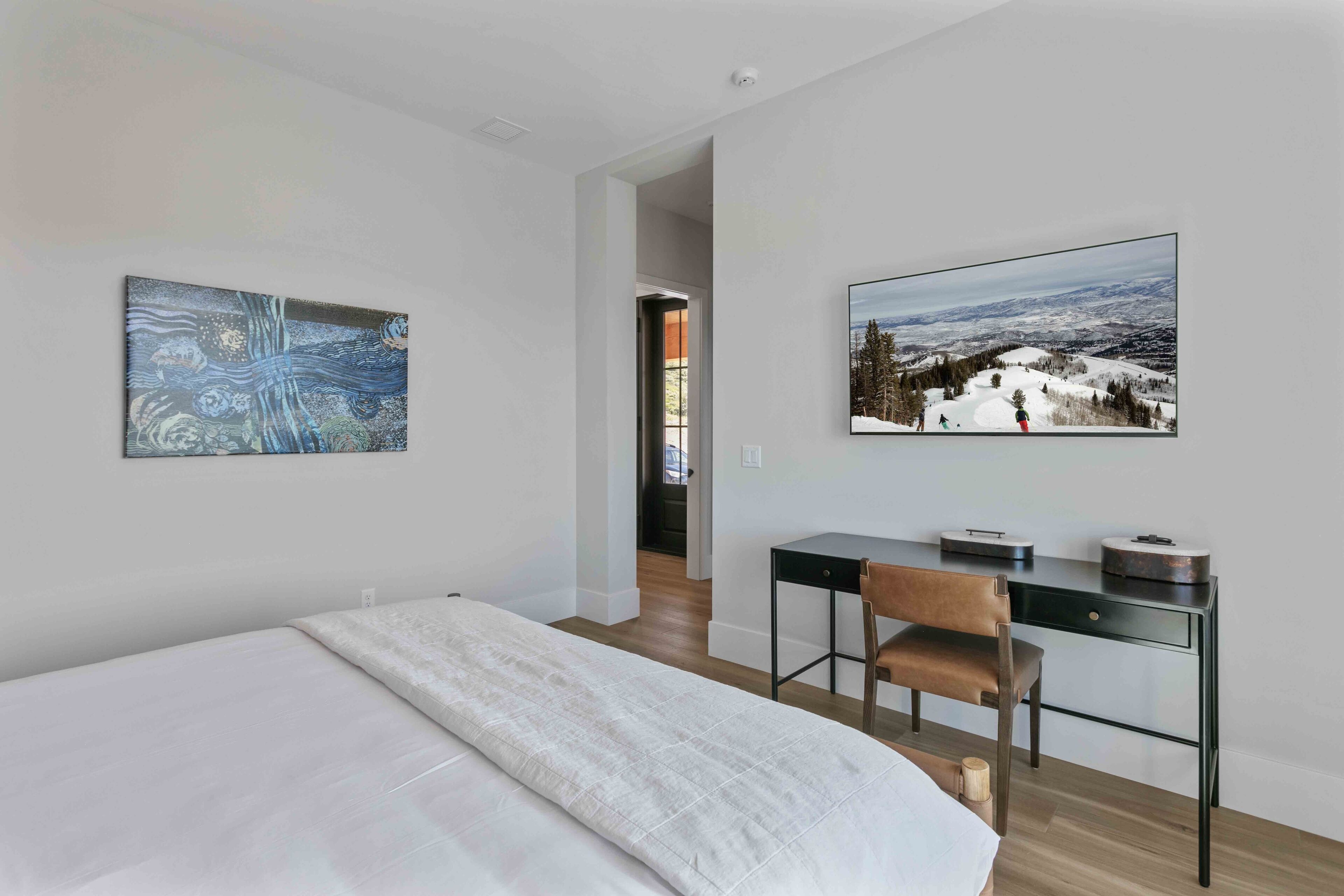 Ein modernes Schlafzimmer mit einem Bett, einem Schreibtisch und einem Stuhl. An den Wänden hängen zwei Bilder.