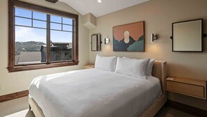 Un dormitorio con una cama grande, una ventana con vistas, un cuadro en la pared y una mesita de noche.