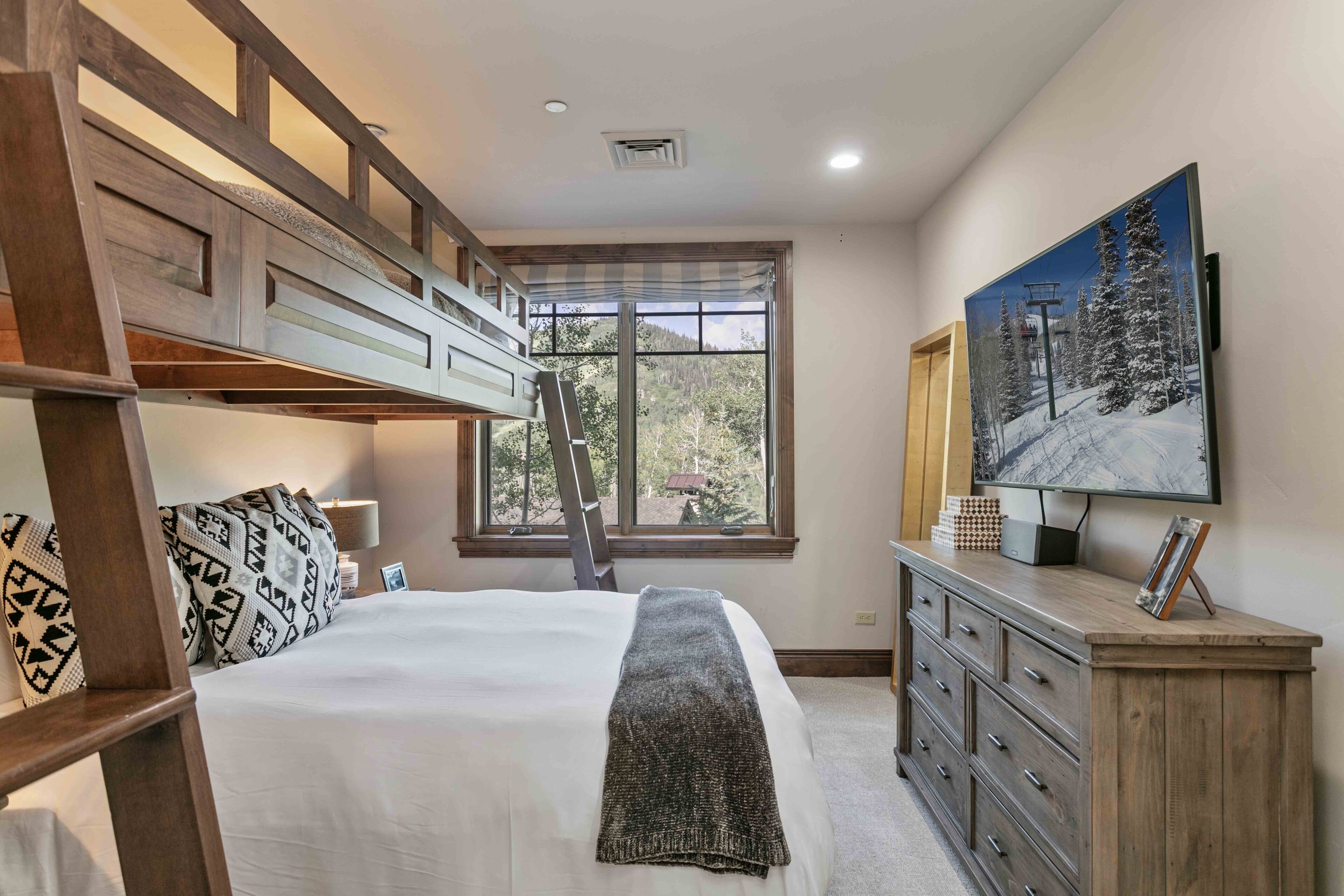 A bedroom with a bunk bed, a dresser, a painting, and a window with a view of trees.