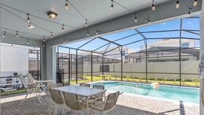 Eine Außenpatio mit Pool, umgeben von Glaswänden und Metallstreben, mit Tisch und Stühlen.