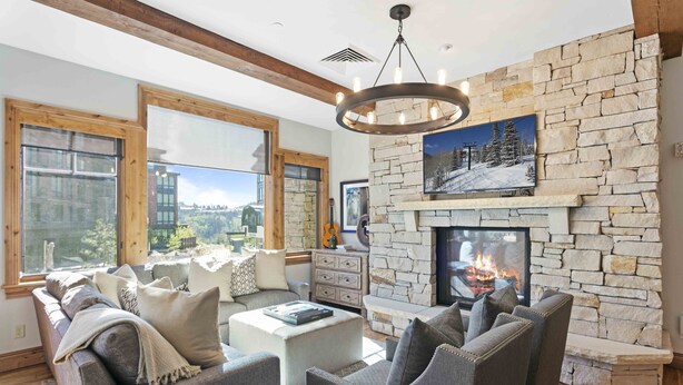 A modern living room with a stone fireplace, large windows, and a cozy seating area. - 302 - Four Bedroom Condo Silver Strike by Deer Valley Resort (Park City)