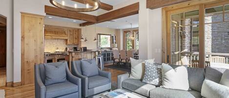A spacious living area with a modern kitchen in the background, a dining area, and a large window providing natural light.