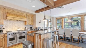 A spacious kitchen with wooden cabinets, a large island, stainless steel appliances, and a dining area with bar stools. - 302 - Four Bedroom Condo Silver Strike by Deer Valley Resort (Park City)