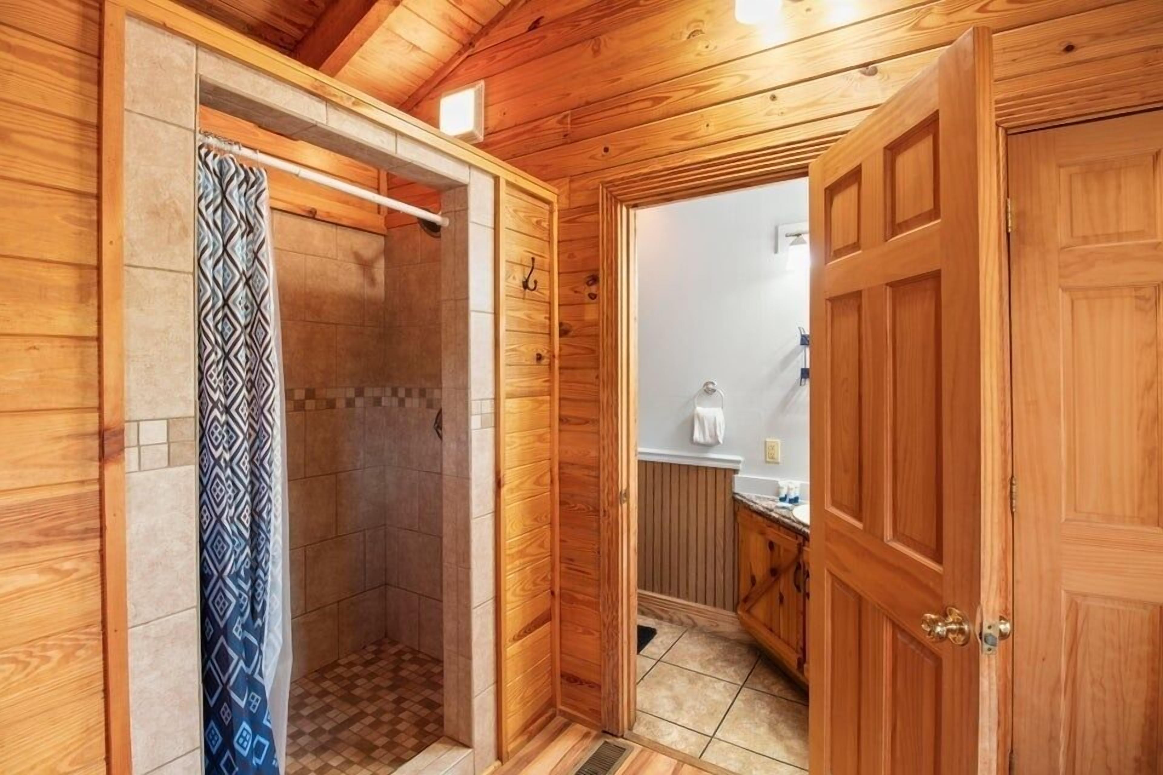 A wooden interior with a shower, a door leading to a bathroom, and a tiled floor.