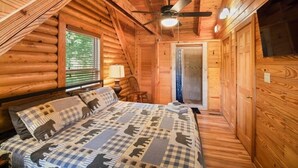 Ein gemütliches Schlafzimmer in einer Holzhütte mit Bett, Deckenventilator und Fenster.
