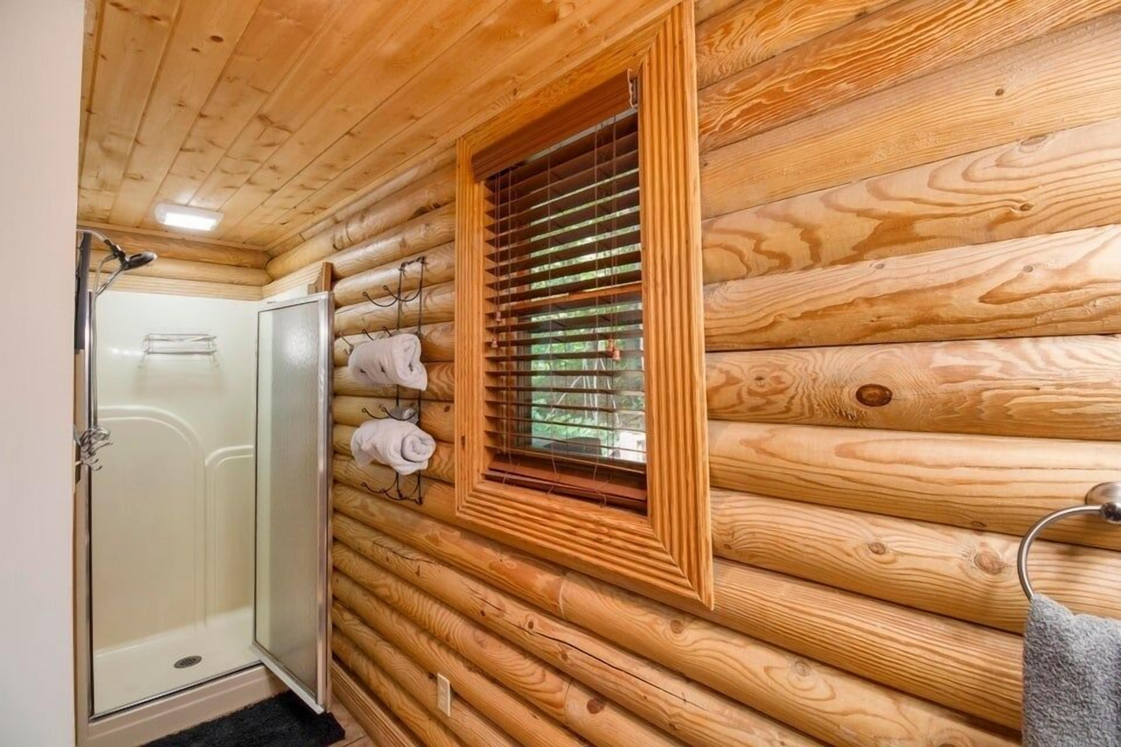 L’intérieur d’une cabane en bois, avec une douche en verre, une fenêtre équipée de stores et un porte-serviettes avec des serviettes.