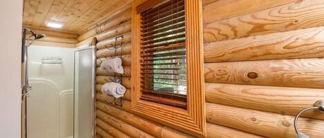 Een houten chalet inrichting met een glazen douchecabine, een raam met zonwering en een handdoekrek met handdoeken.