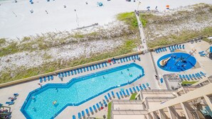 An aerial view of a resort with a large swimming pool, beach area, and a separate pool with a slide. - Phoenix V 1009 2 Bedroom Condo (Orange Beach)