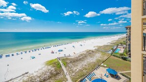 A beach view from a balcony with a clear sky, a sandy beach, and a pool area. - Phoenix V 1009 2 Bedroom Condo (Orange Beach)