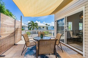 Um alpendre coberto com mesa e cadeiras, vista para casas vizinhas e porta de vidro deslizante que dá para uma área interna com cadeiras.