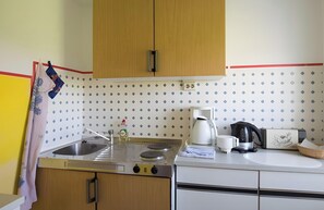 A kitchen with wooden cabinets, a sink, a stove, a kettle, and a coffee maker.