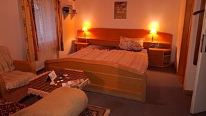 Ein gemütliches Zimmer mit einem hölzernen Bett, zwei Nachttischlampen, einem kleinen Tisch mit Lampe und einem Sessel.