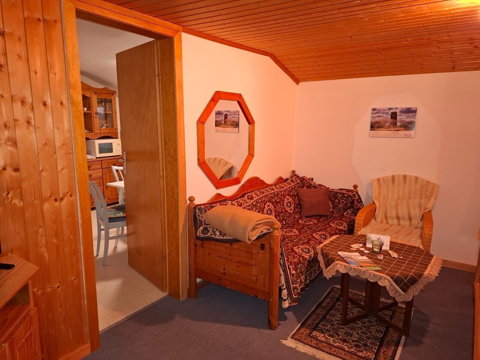 Een gezellige kamer met houten plafond, een bank, een stoel, een tafeltje en een kast met een magnetron.