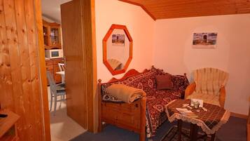 Een gezellige kamer met houten plafond, een bank, een stoel, een tafeltje en een kast met een magnetron.