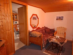 Une pièce chaleureuse avec un plafond en bois, un canapé, un fauteuil, une petite table et un meuble contenant un four à micro-ondes.