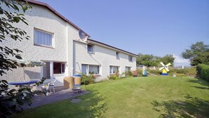 Ein zweistöckiges Wohngebäude mit Backsteinfassade, Satellitenschüssel und Windrad im Garten.