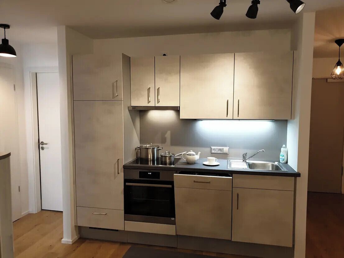 Een moderne keuken met roestvrijstalen apparatuur, een vaatwasser en een aanrecht met waterkoker en kopjes.