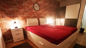 A modern bedroom with a brick wall, a bed with a red bedspread, bedside tables with lamps, and a large mirror. - Top equipped apartment in a central location in Freilassing (Freilassing)