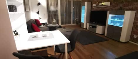 Een moderne woonkamer met een witte tafel, zwarte stoelen, een grijze bank en een tv-meubel.