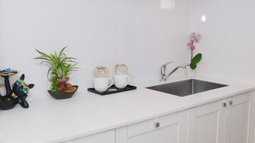 Une cuisine moderne avec des meubles blancs, un évier en acier inoxydable et une hotte intégrée.