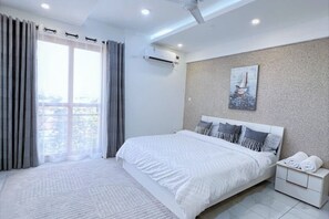 Quarto moderno com uma cama grande, vista da cidade e um quadro na parede.