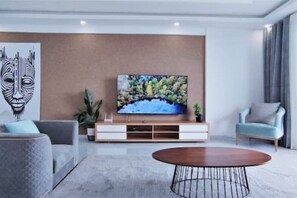 Uma sala de estar moderna com televisão de tela plana presa a um armário de madeira, um sofá cinza, uma mesa de centro redonda e uma poltrona azul.