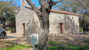 A stone building with a tiled roof, a mailbox, and a tree in front. - The Scola of Pirazzolu Retreat (Olbia)