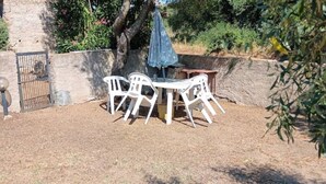 An outdoor seating area with white plastic chairs and a table, surrounded by a stone wall and greenery. - The Scola of Pirazzolu Retreat (Olbia)