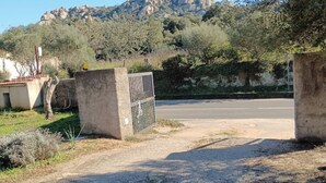 A rural road with a gated entrance, a dirt path, and a mountainous backdrop. - The Scola of Pirazzolu Retreat (Olbia)
