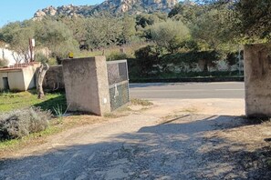 A rural road with a gated entrance, a dirt path, and a mountainous backdrop. - The Scola of Pirazzolu Retreat (Olbia)