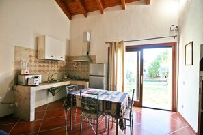 A kitchen with a dining table, chairs, a microwave, a sink, cabinets, and a window with curtains. - The Scola of Pirazzolu Retreat (Olbia)