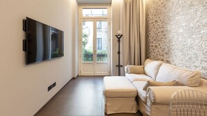 Un salon moderne avec un téléviseur à écran plat, un canapé, un pouf, une lampe sur pied et un mur décoré d’un motif.