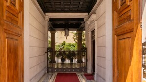 Un couloir avec des portes en bois, des colonnes et une moquette rouge menant à une porte.