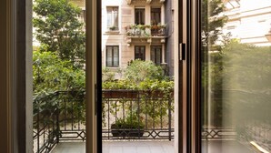 Une vue depuis un balcon doté d’une rambarde en métal, donnant sur une cour intérieure agrémentée de plantes en pot et sur un immeuble avec des balcons.
