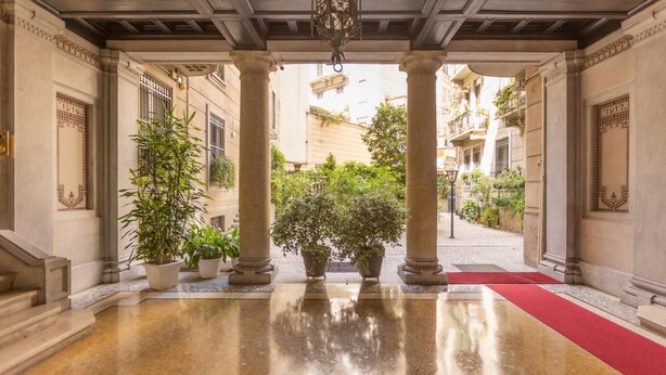 Une entrée imposante avec un sol en marbre poli, des plantes en pot et un tapis rouge menant à une cour intérieure.