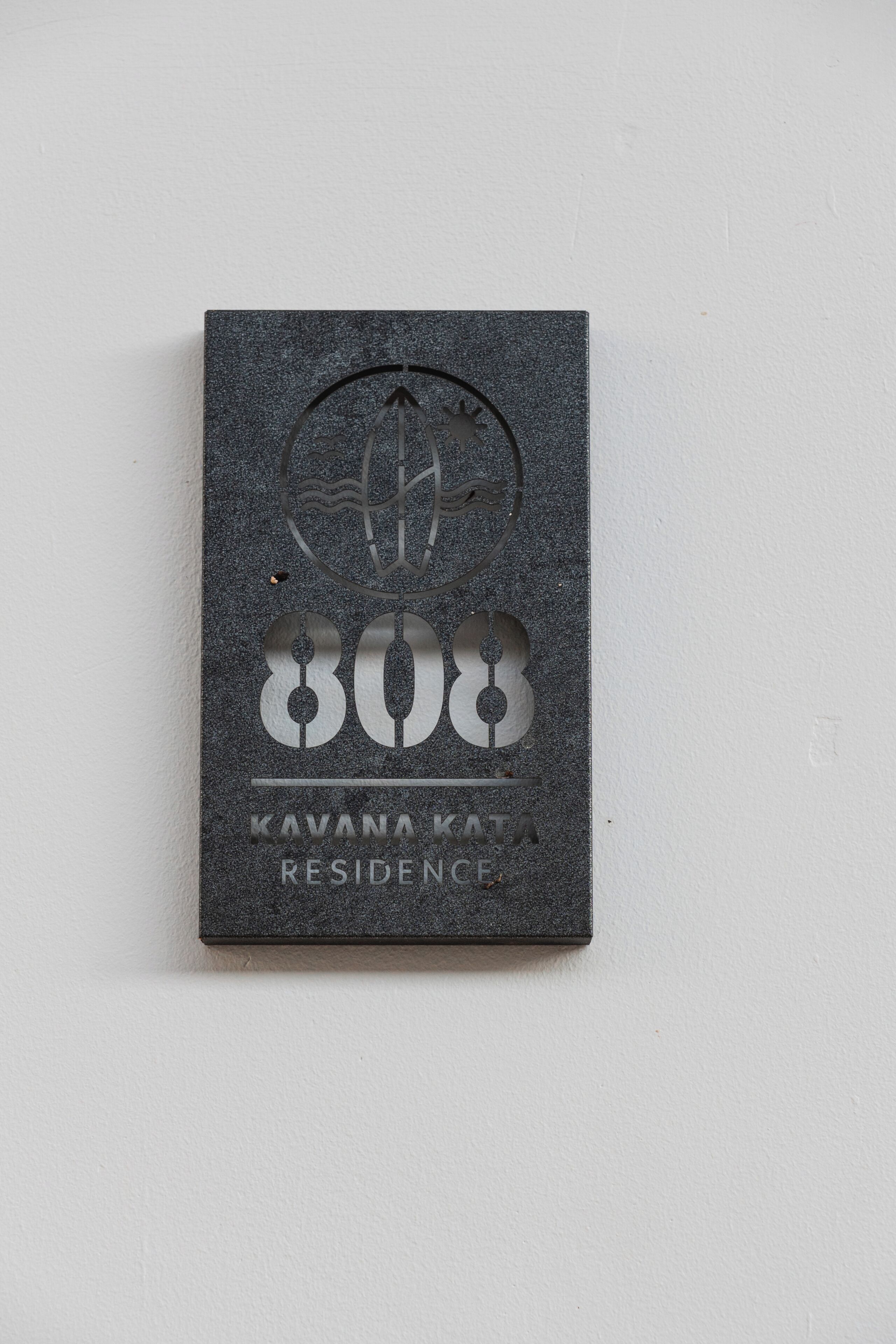 A dark, textured plaque with a circular emblem, the number '808', and the text 'KAVANA KATA RESIDENCE'.