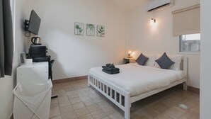 A bedroom with a bed, bedside table, lamp, air conditioning unit, and a desk with a computer and a kettle. - Kavana Kata Residence (Karon)