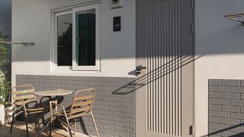 Un patio con mesa y sillas, una puerta con ventanal y un aplique de pared.