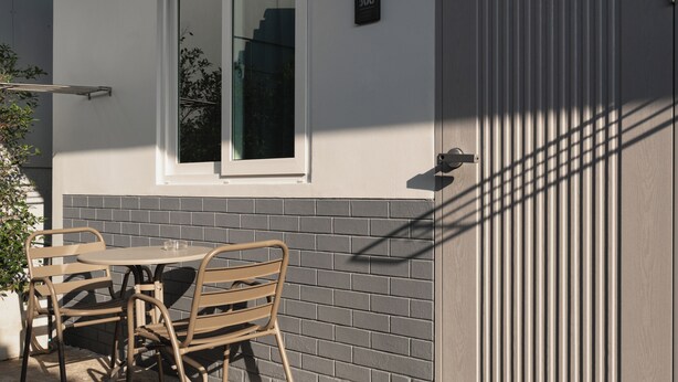 A patio with a table and chairs, a window, and a door with a vertical panel. - Kavana Kata Residence (Karon)