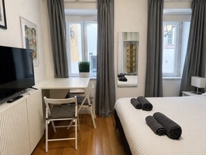 Ein Hotelzimmer mit Bett, Schreibtisch, Stuhl, Fernseher und einem Fenster mit Vorhängen.
