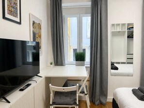 Ein modernes Schlafzimmer mit Bett, Schreibtisch, Fernseher und einem Fenster mit Vorhängen.