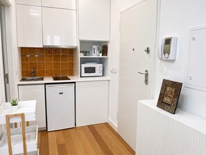 Een compacte keuken met witte kastjes, een magnetron, een kleine koelkast en een wit aanrecht.